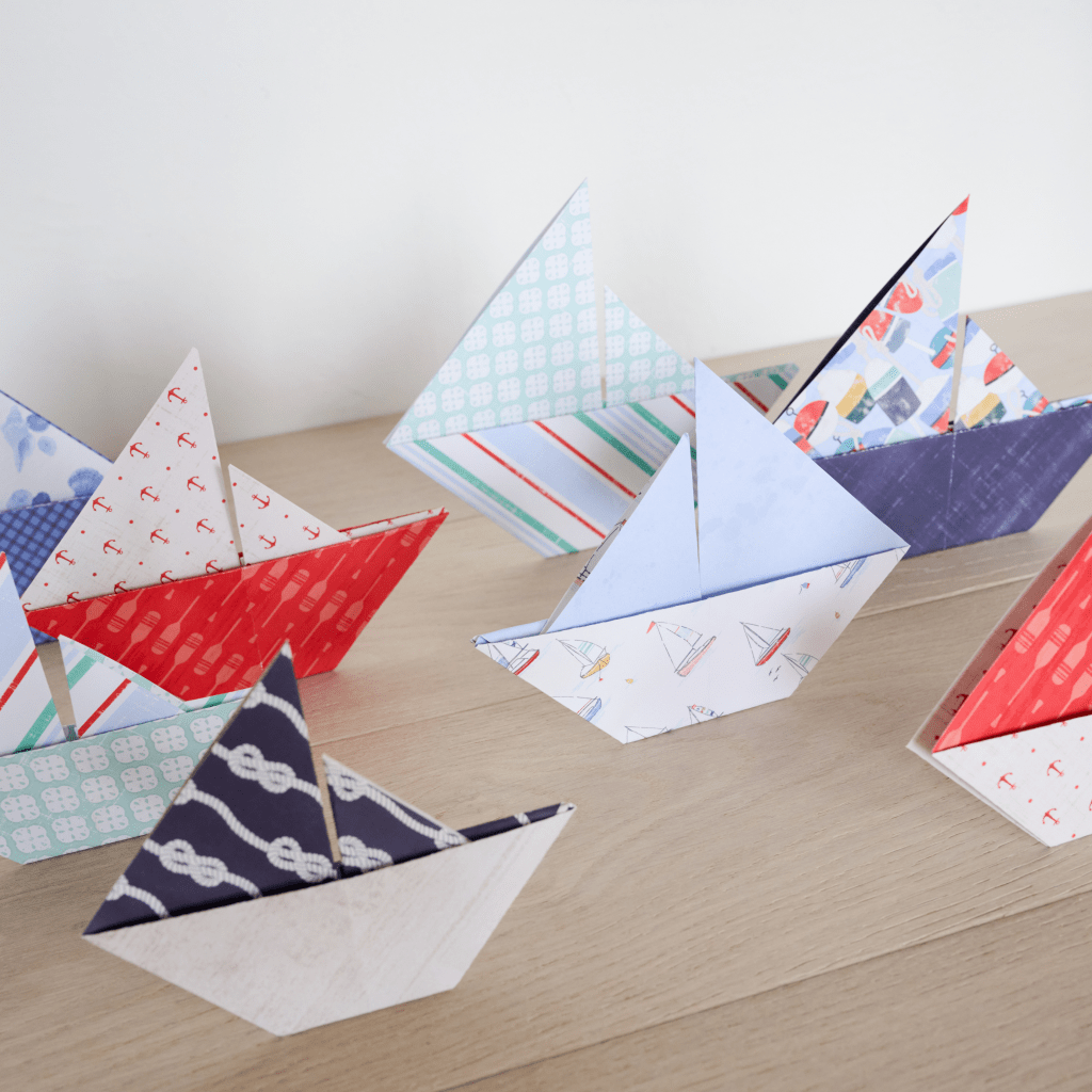 A collection of colorful paper boats made from patterned origami paper, displayed on a wooden surface.