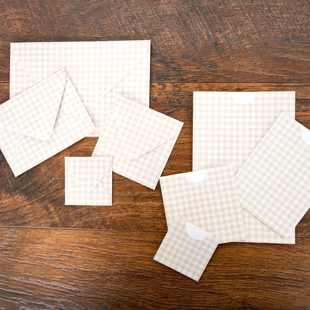 A collection of beige and white checked envelopes of various sizes arranged on a wooden surface.