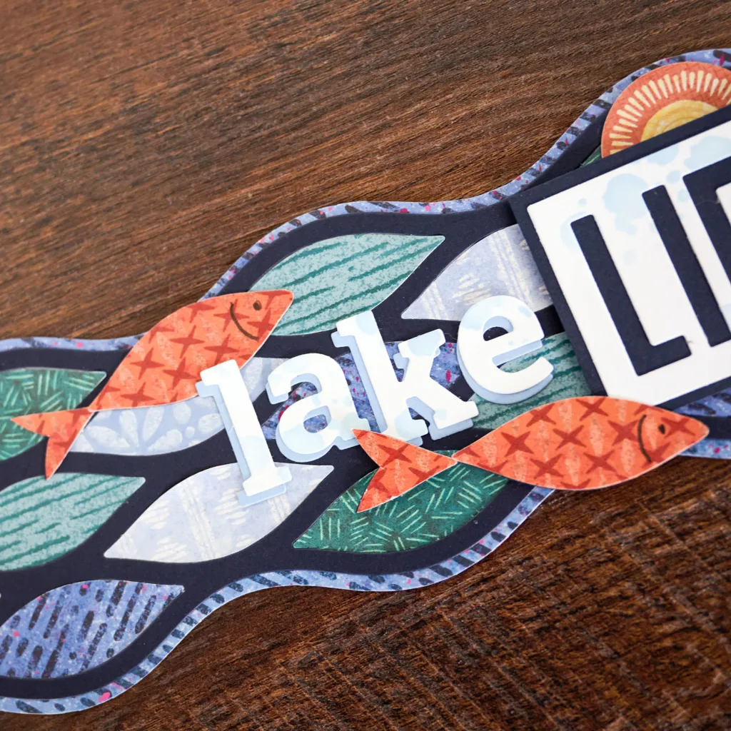 Close-up of a decorative design featuring the word 'lake' in white letters, surrounded by colorful fish and leaves on a dark background.