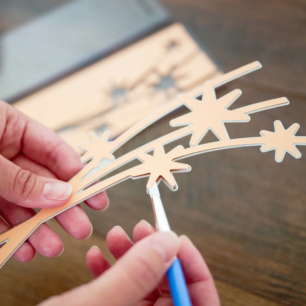 Close-up of hands holding a decorative cutout with star shapes, while using a brush to apply paint or finish on it.
