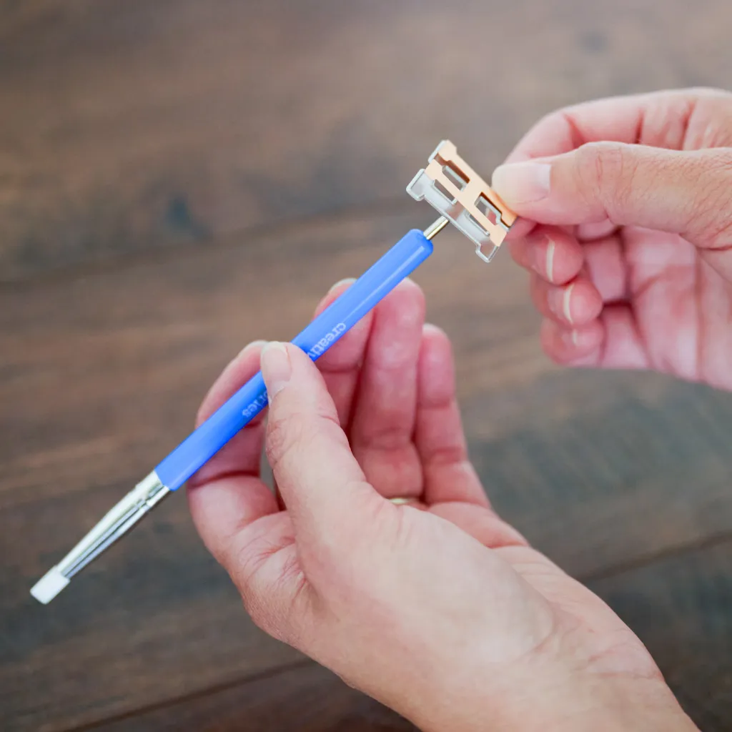 A person holding a blue pen in one hand and a pencil sharpener in the other hand, with a wooden table surface visible in the background.