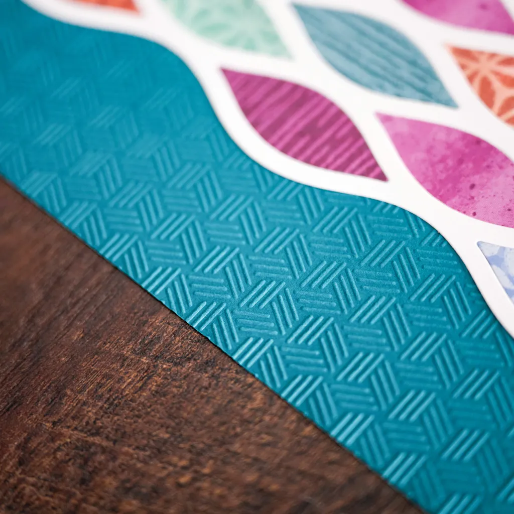 Close-up of a textured turquoise surface with a geometric pattern, bordered by colorful leaf-shaped cutouts against a wooden background.