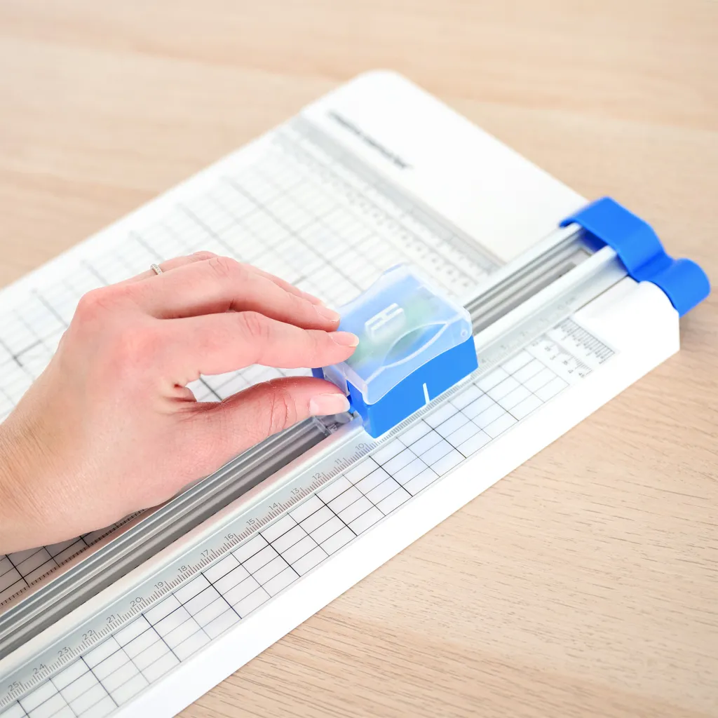 A hand positioned on a blue paper cutter, adjusting the measuring guide on a cutting mat.