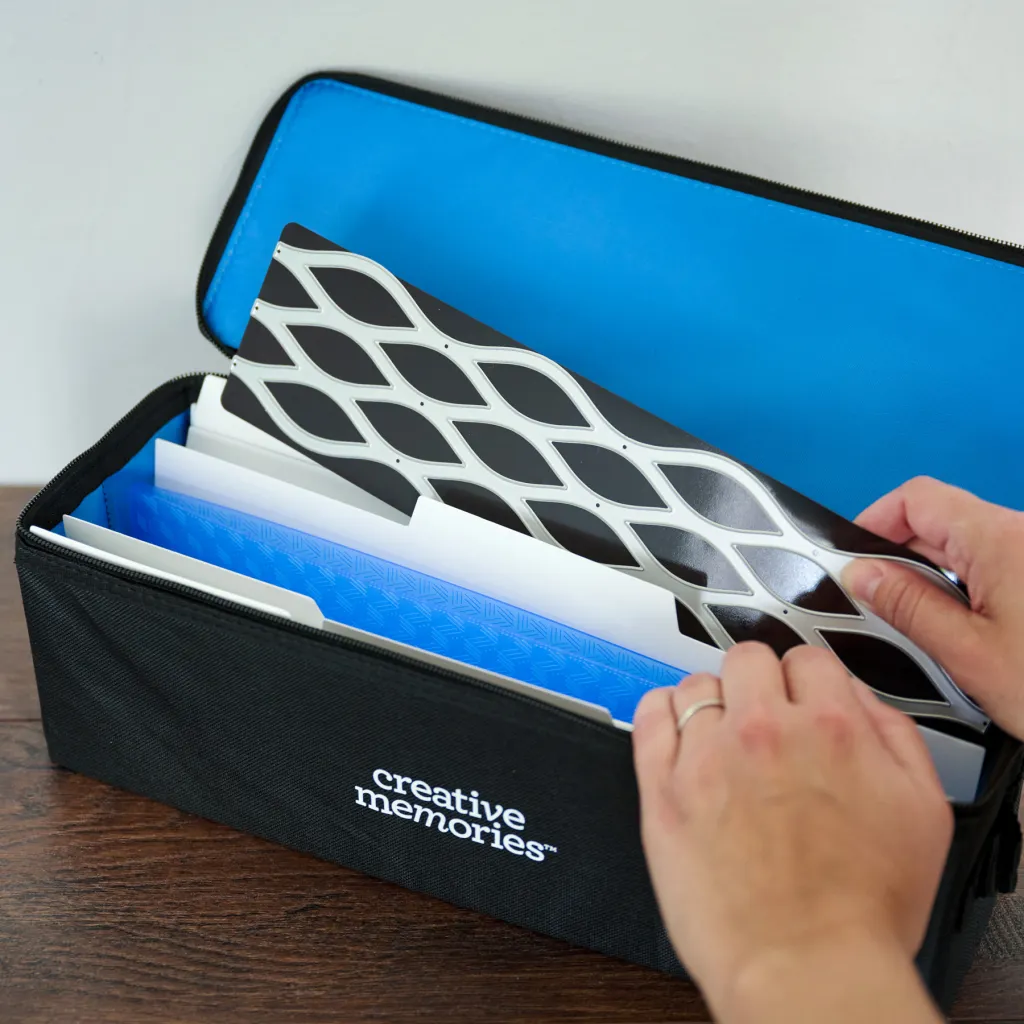 A person is opening a black zippered case labeled 'creative memories' that contains various colorful folders and organizer sheets, with a blue interior.